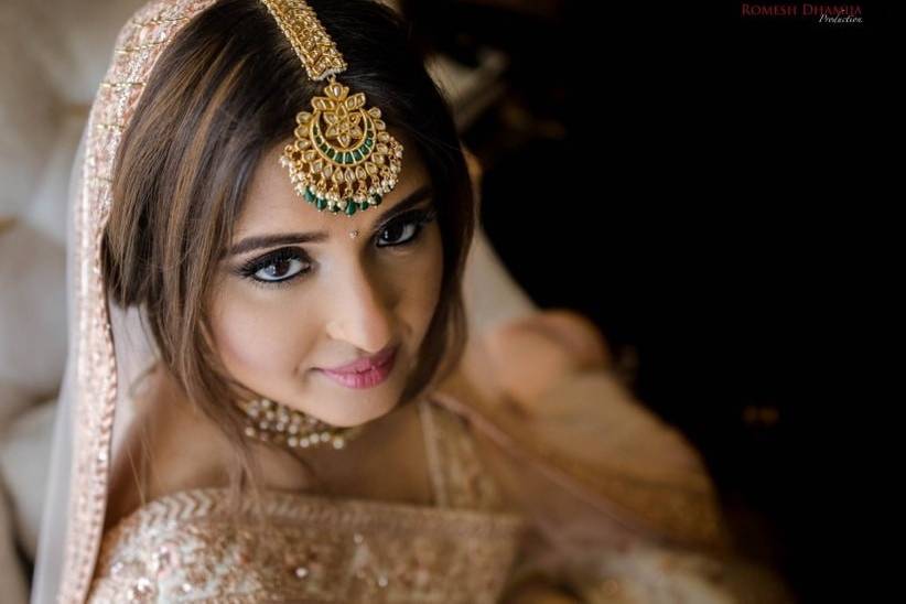 Elegant bride wearing a designer maang tikka adorned with gemstones, showcasing Affordable Luxury jewelry by Poorni Fab.